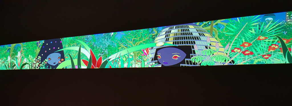 Chiho Aoshima City Glow Opening scene of City Glow video projection. The projected animation is primarily green, covered with animated plants. In the foreground, there are two anthropomorphic buildings with anime-like faces.